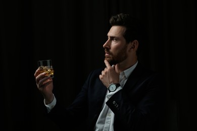 Handsome man in suit holding glass of whiskey on black background