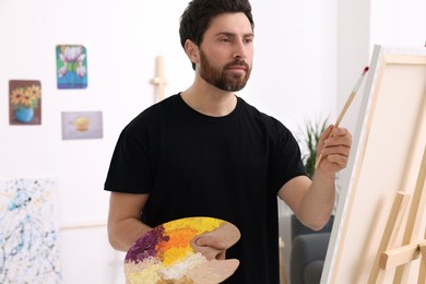 Photo of Man painting in studio. Using easel to hold canvas