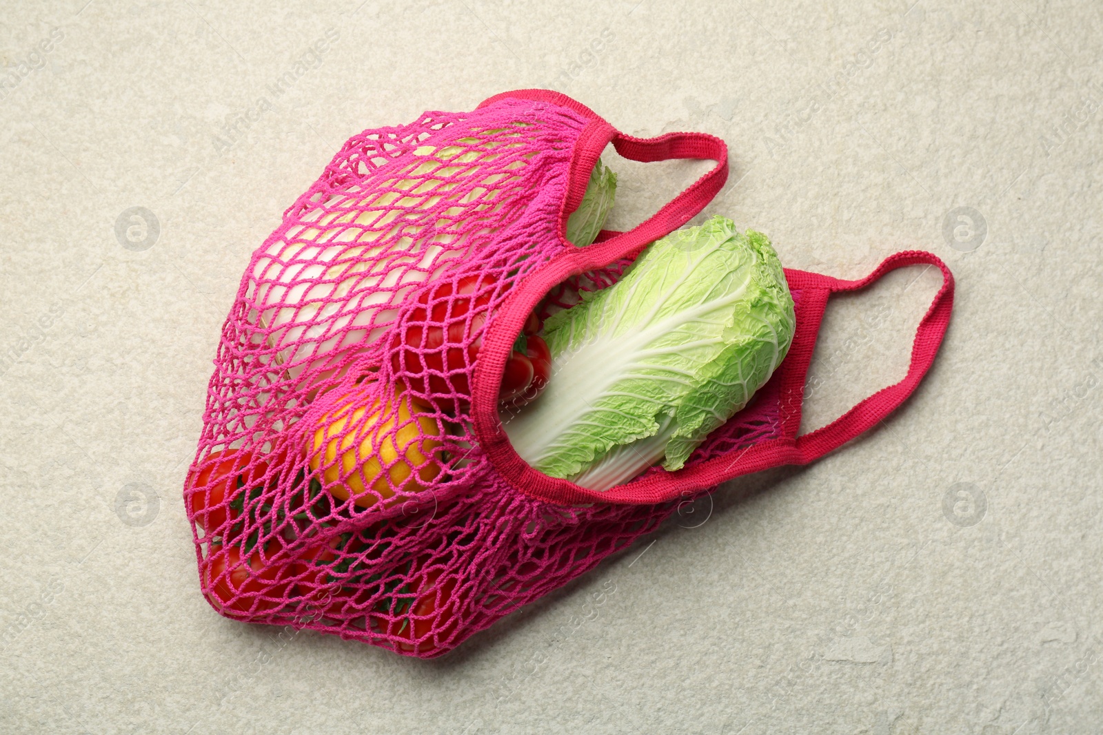 Photo of Fresh Chinese cabbage and other products in string bag on light textured table, top view