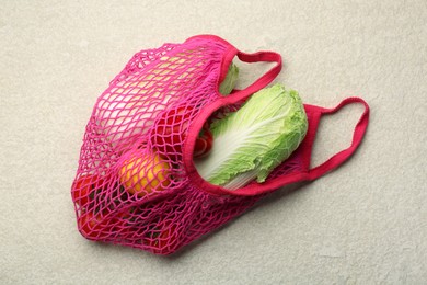 Photo of Fresh Chinese cabbage and other products in string bag on light textured table, top view