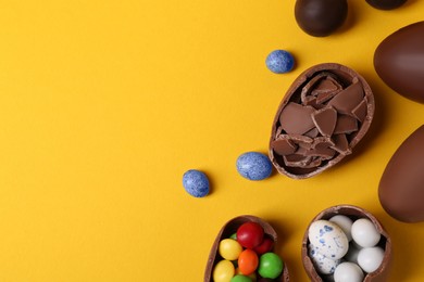 Photo of Whole and halves of chocolate eggs with colorful candies on yellow background, flat lay. Space for text