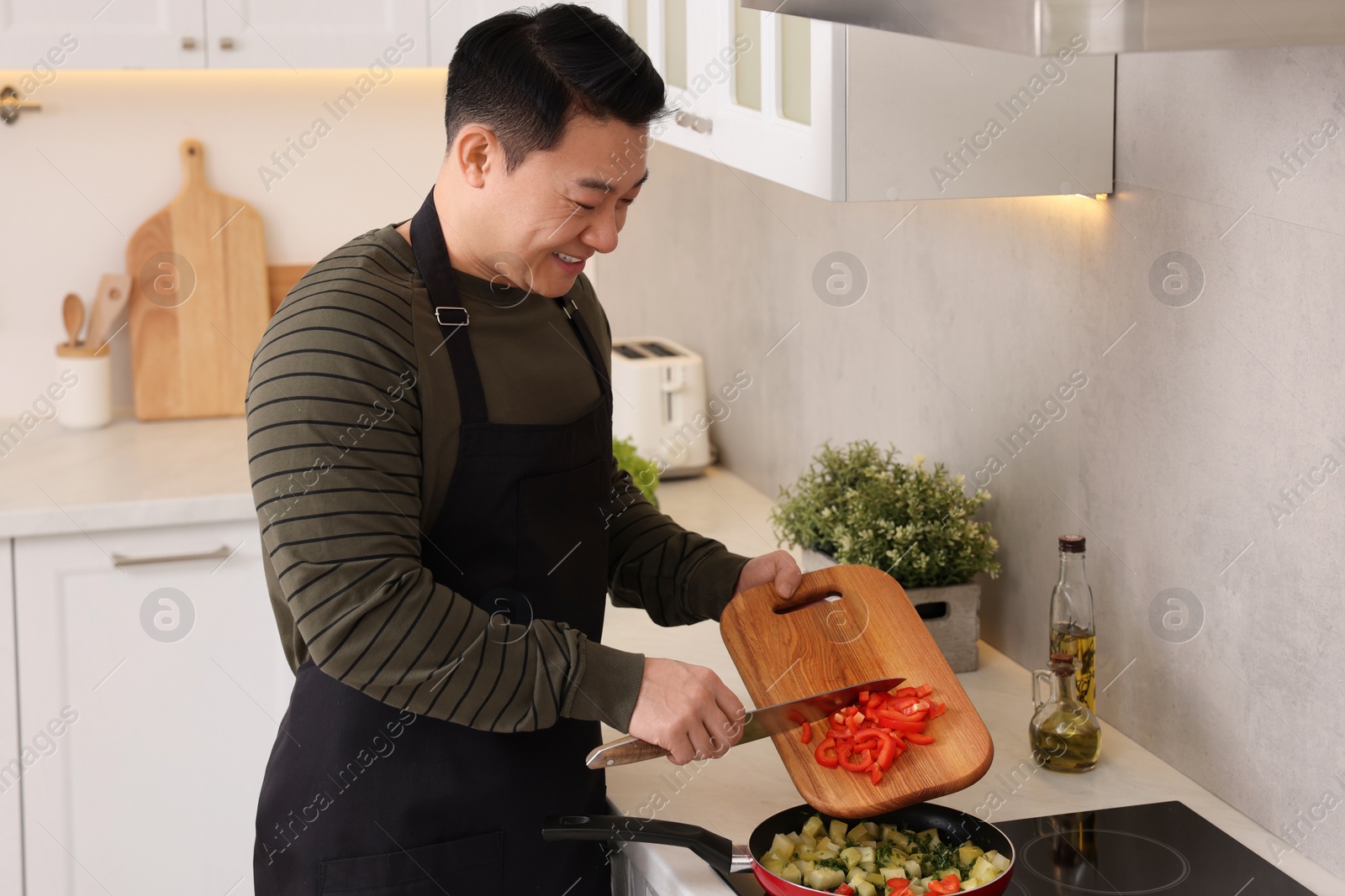 Photo of Cooking process. Man adding cut bell pepper into frying pan in kitchen