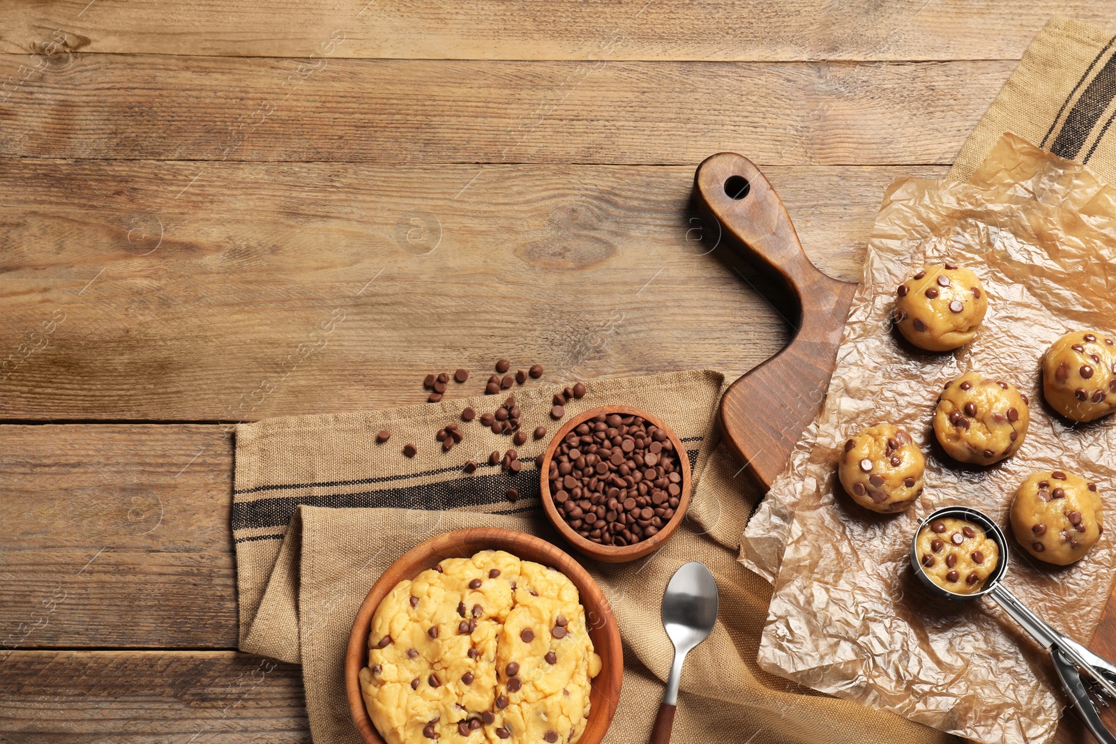 Photo of Bowl with dough and uncooked chocolate chip cookies on wooden table, flat lay. Space for text