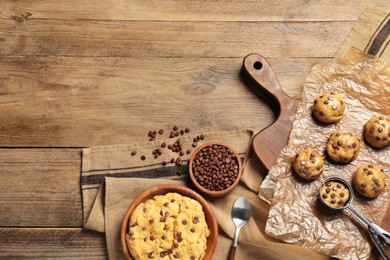 Photo of Bowl with dough and uncooked chocolate chip cookies on wooden table, flat lay. Space for text