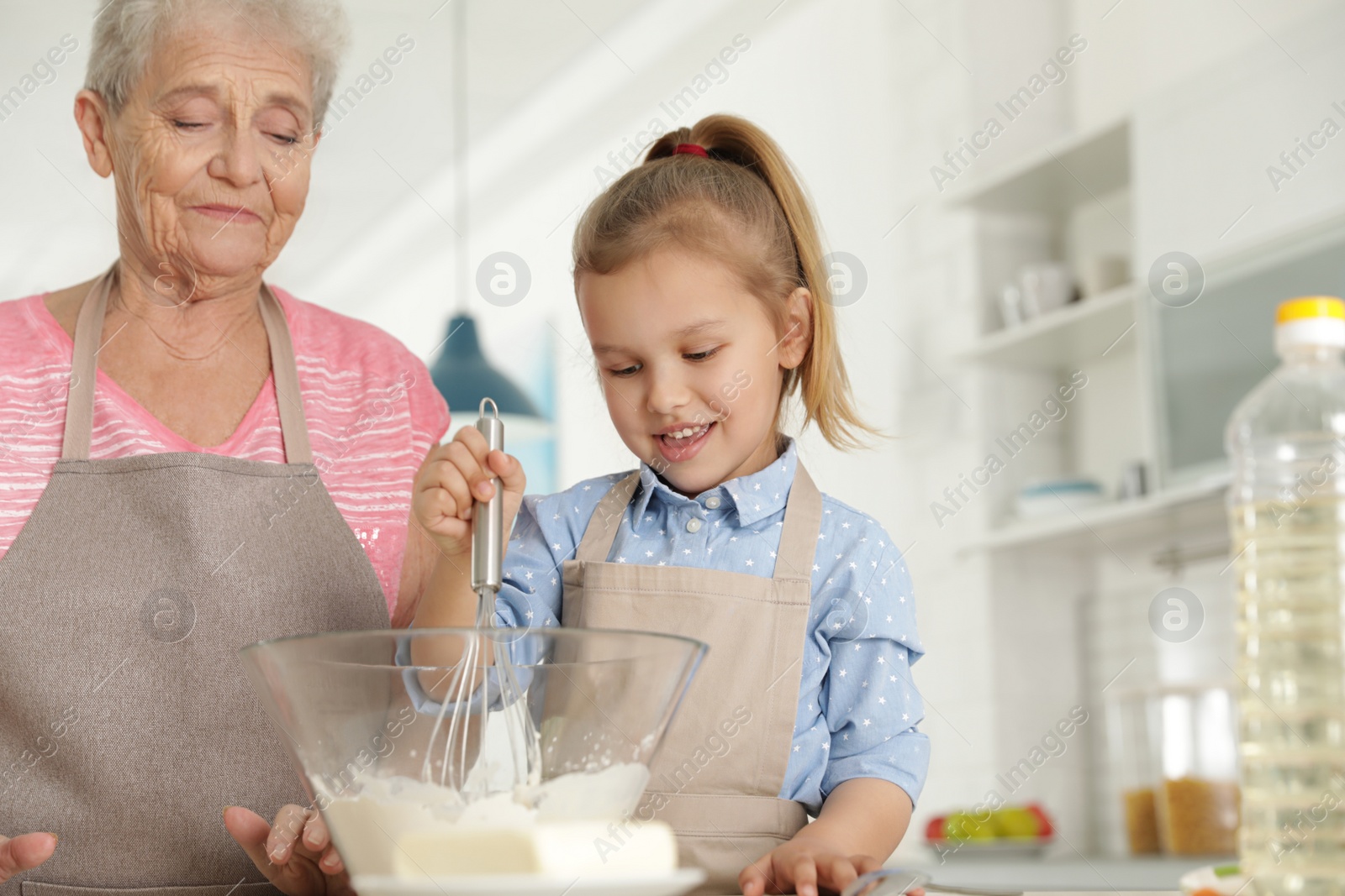 Photo of Cute girl and her grandmother cooking in kitchen