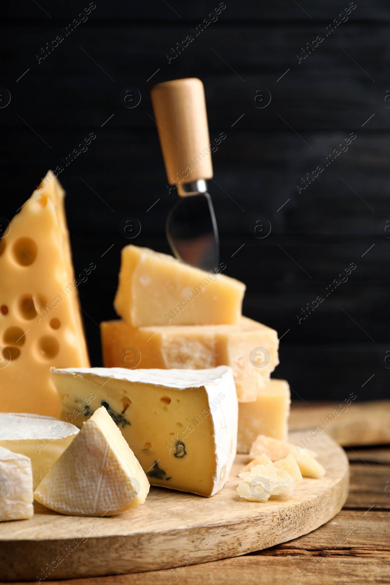 Photo of Different sorts of cheese and knife on wooden table against black background, closeup