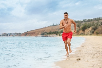 Photo of Handsome male lifeguard running on sandy beach