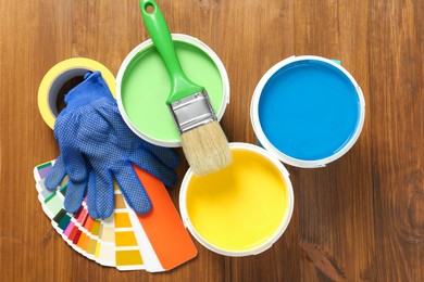 Photo of Buckets of paints, palette and decorator's accessories on wooden background, flat lay