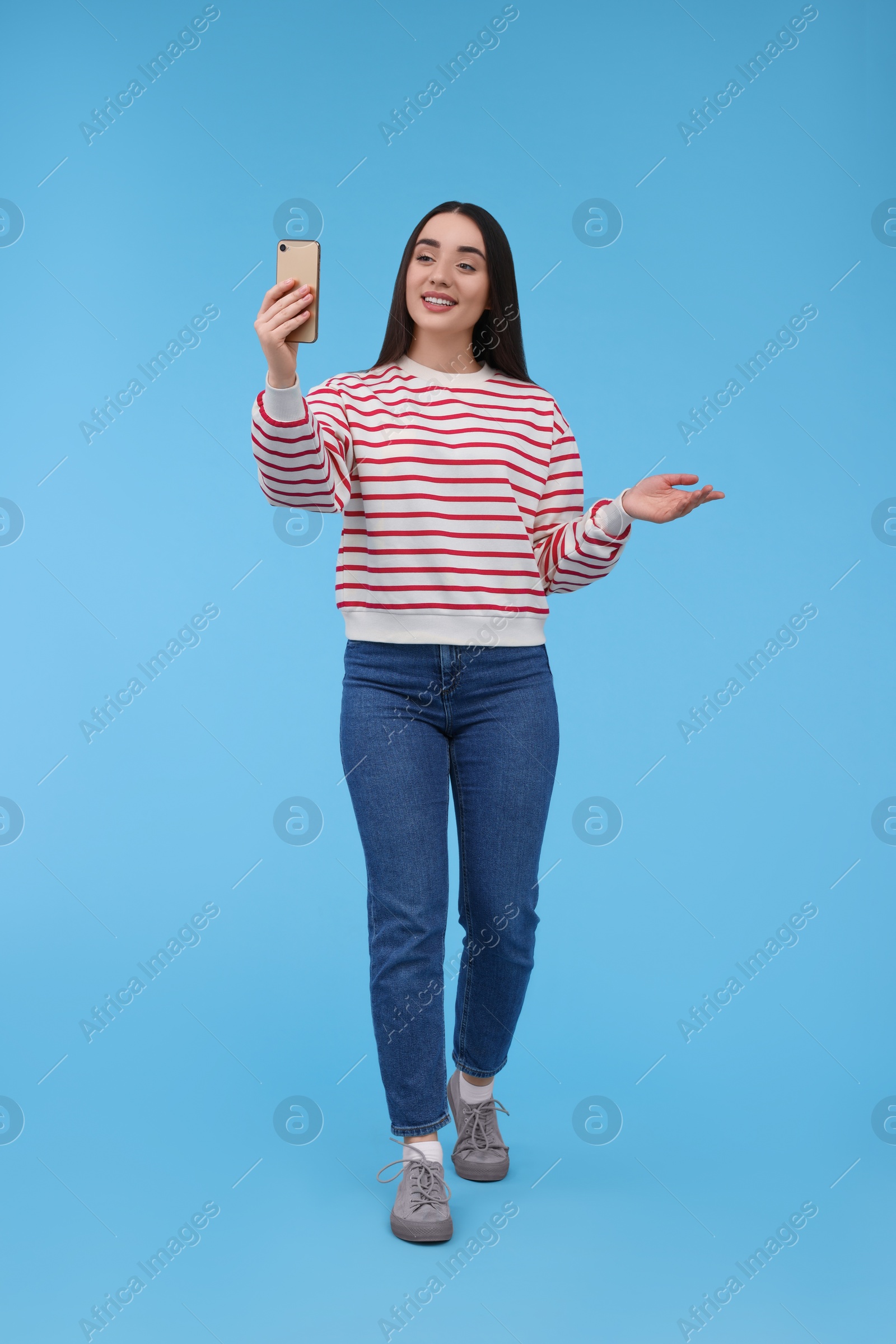 Photo of Smiling young woman taking selfie with smartphone on light blue background