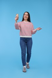 Photo of Smiling young woman taking selfie with smartphone on light blue background