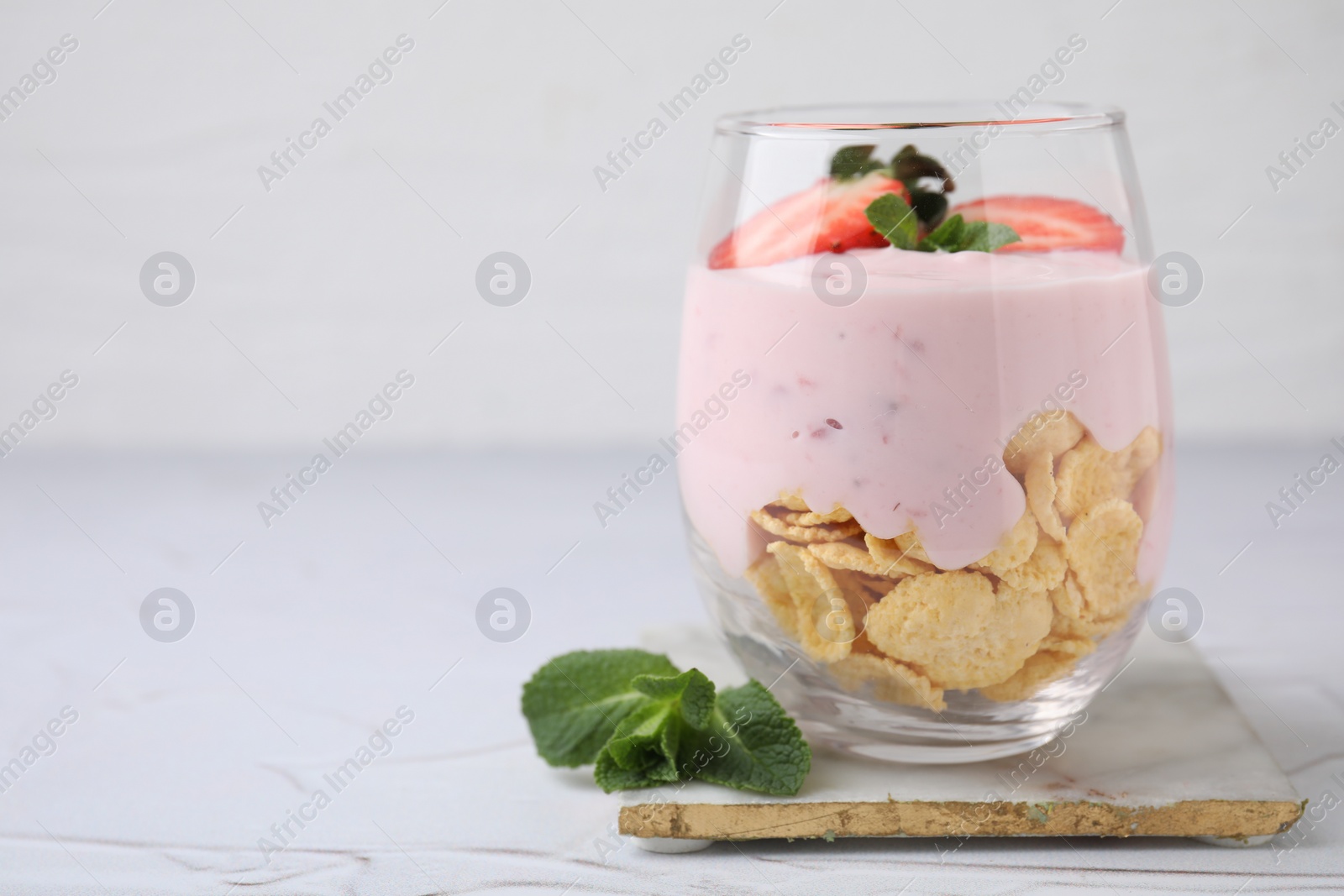 Photo of Glass with yogurt, strawberries and corn flakes on white textured table. Space for text