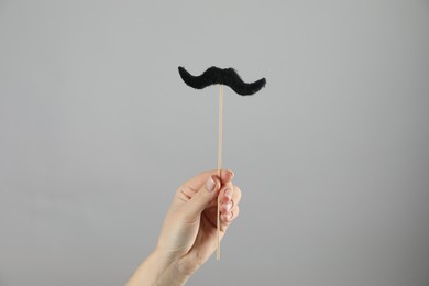 Woman with fake paper mustache on gray background, closeup