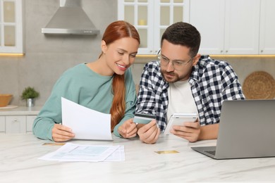 Photo of Couple with credit card calculating taxes for online payment at table in kitchen