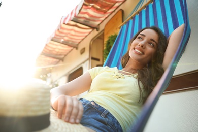 Photo of Young woman with hat resting in hammock near motorhome outdoors on sunny day