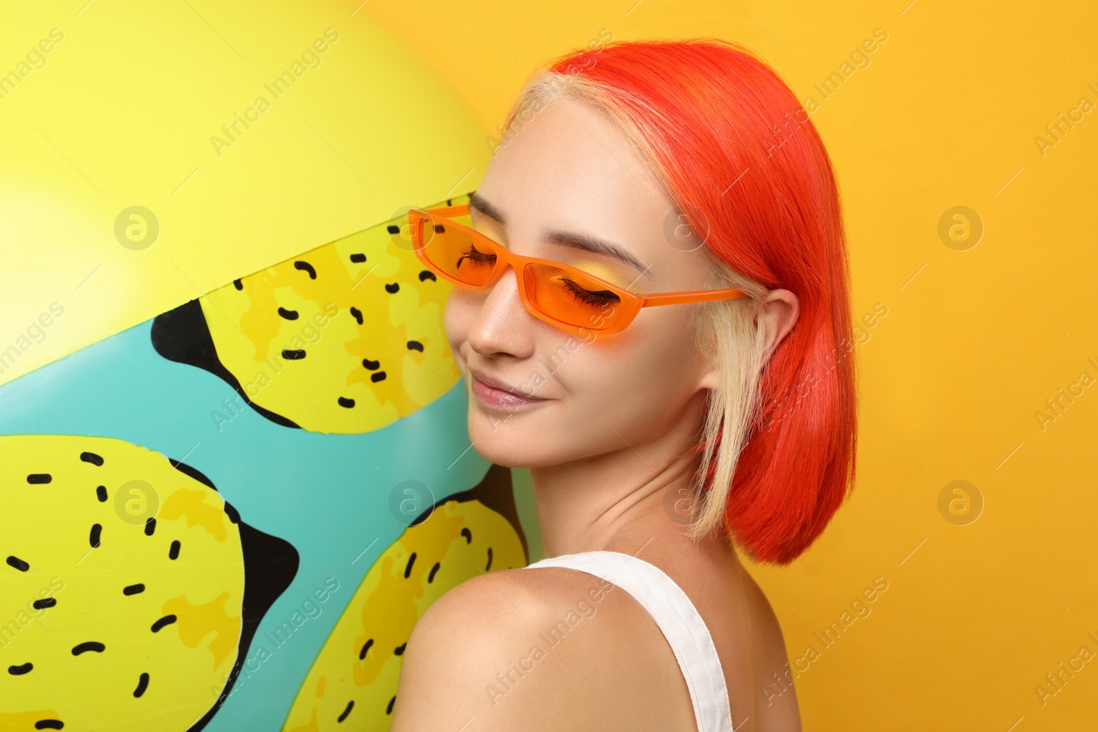 Photo of Beautiful young woman with bright dyed hair and inflatable ball on orange background