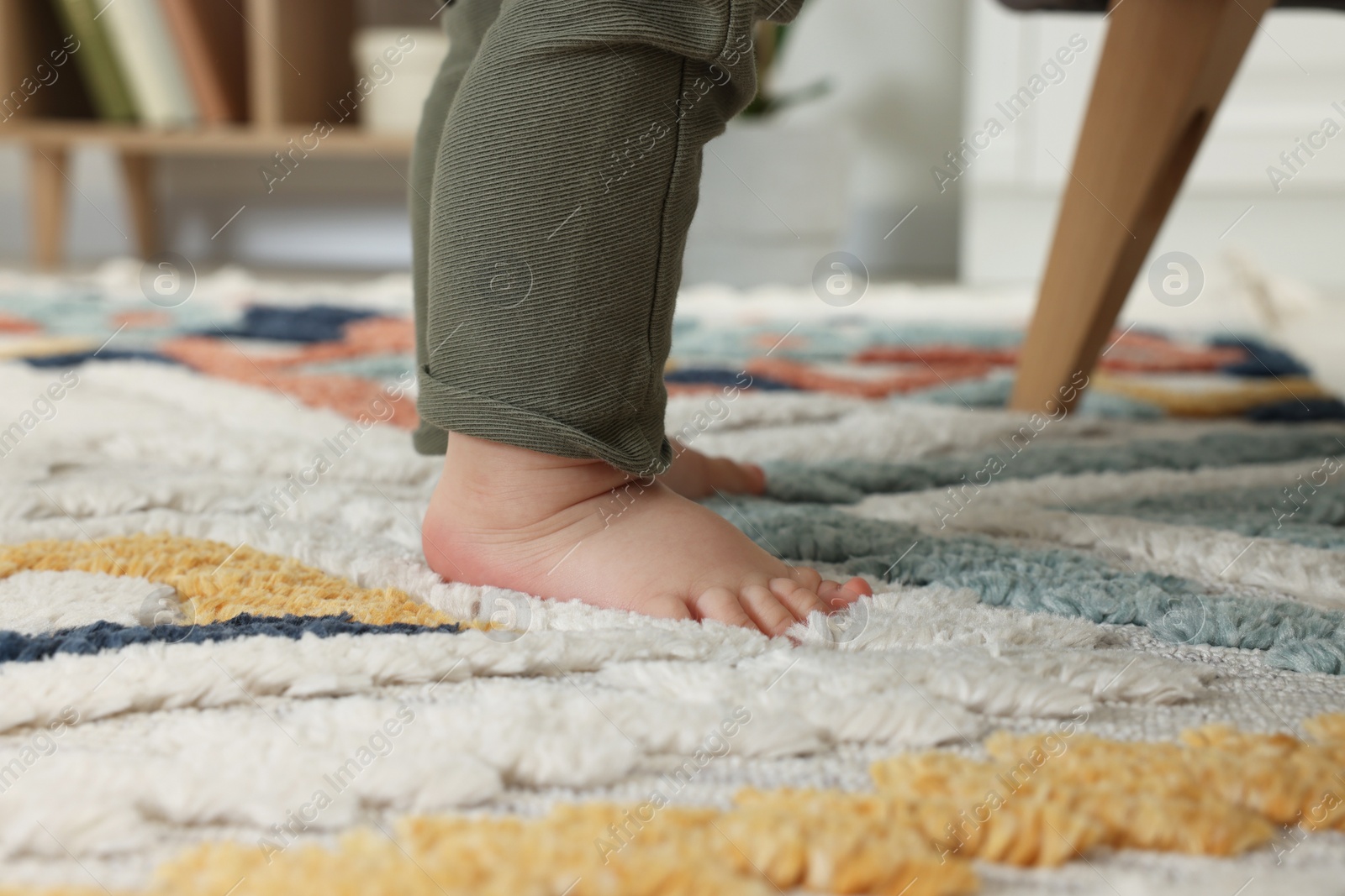 Photo of Baby standing on soft colorful carpet indoors, closeup