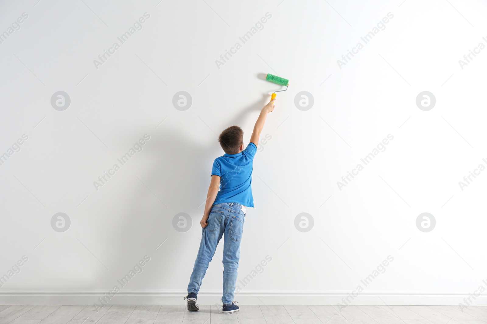 Photo of Little child painting with roller brush on white wall indoors