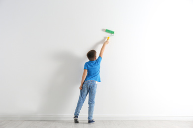 Little child painting with roller brush on white wall indoors