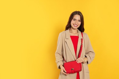 Beautiful young woman in fashionable outfit with stylish bag on yellow background, space for text