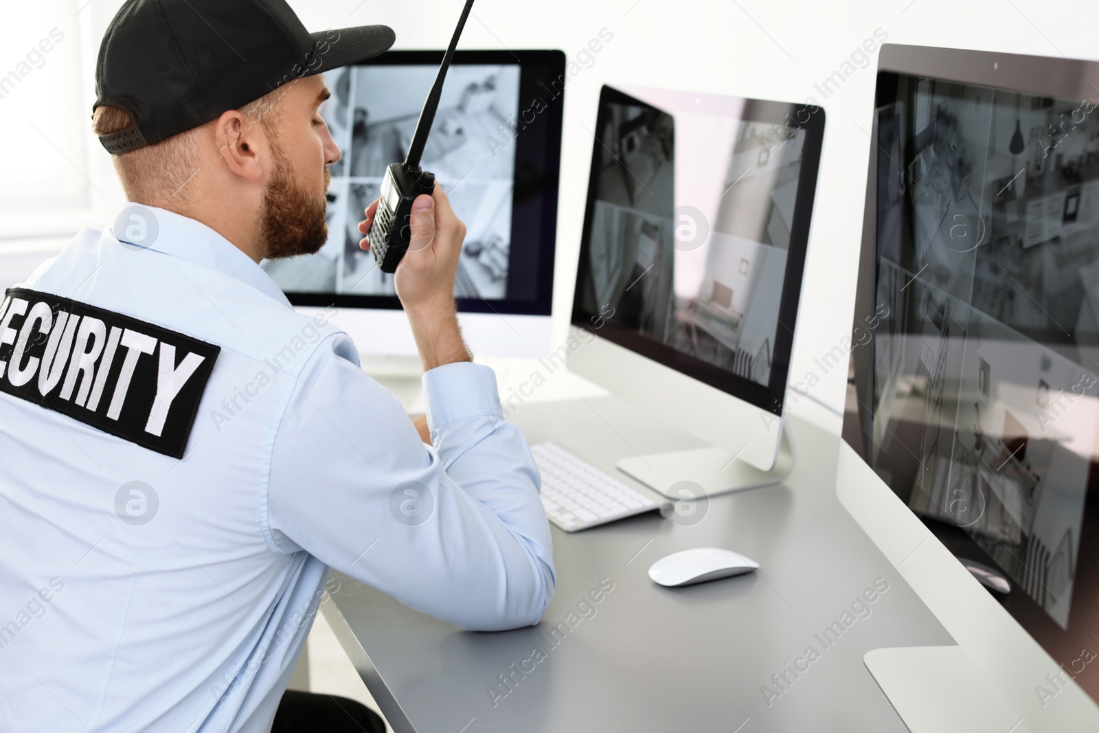 Photo of Male security guard with portable transmitter monitoring home cameras indoors