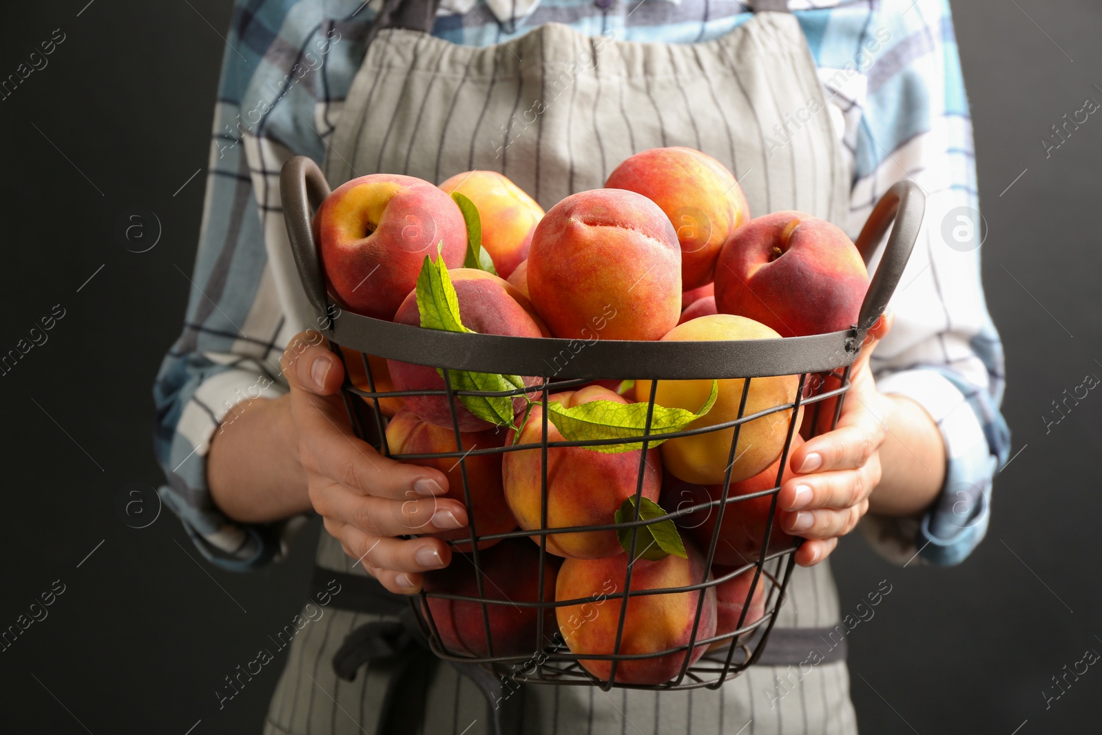 Photo of Woman with fresh sweet peaches in metal basket, closeup