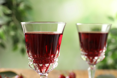 Photo of Delicious cherry wine on blurred green background, closeup