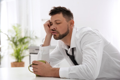 Photo of Sleepy man with cup of drink at home in morning