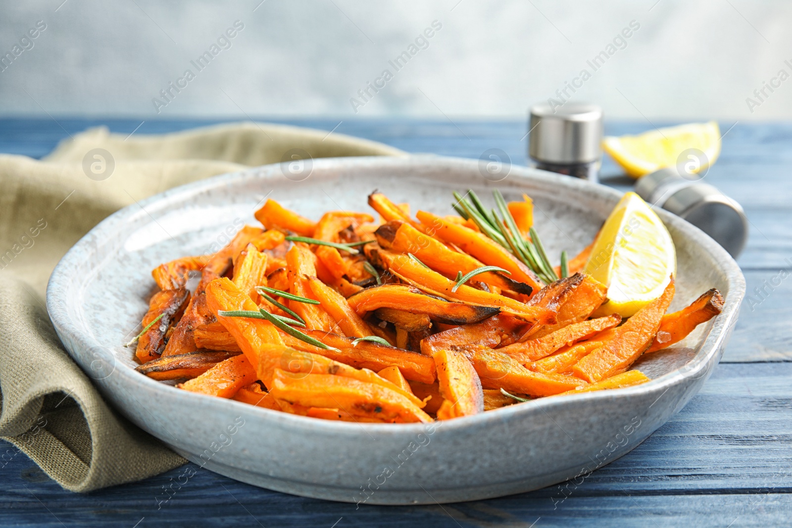 Photo of Plate with baked sweet potato slices, rosemary and lemon on wooden table, closeup