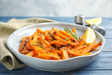 Photo of Plate with baked sweet potato slices, rosemary and lemon on wooden table, closeup