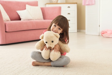 Photo of Cute little girl playing with teddy bear at home