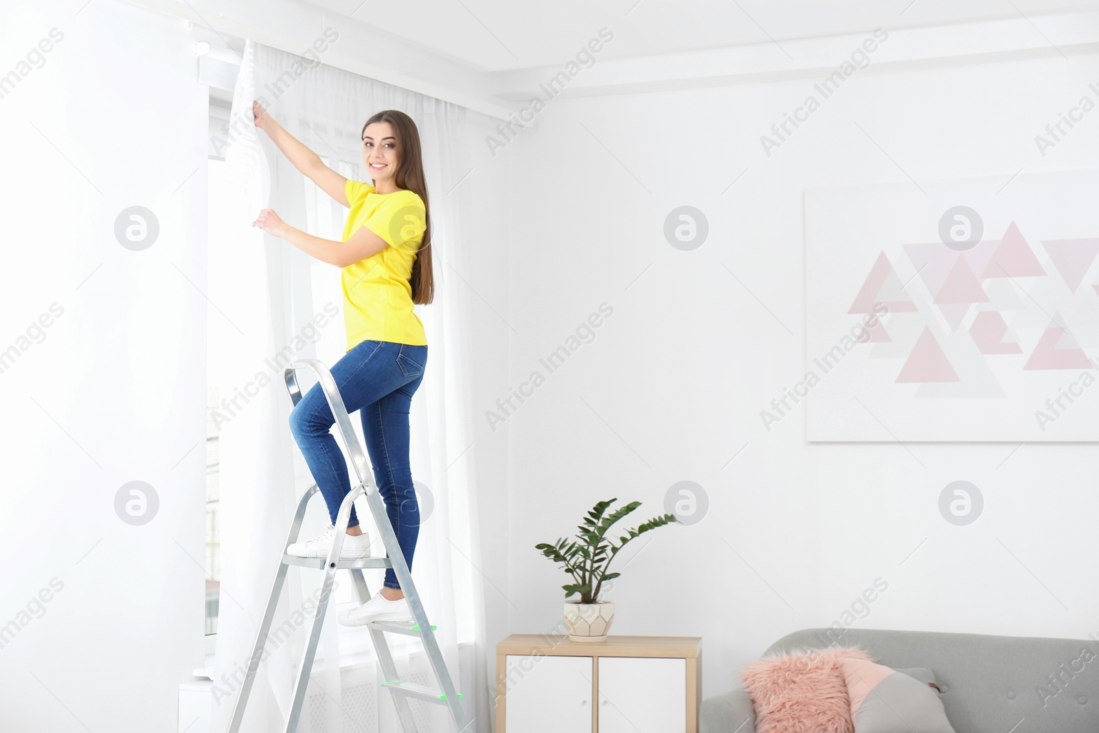 Photo of Young woman hanging window curtain in room. Space for text