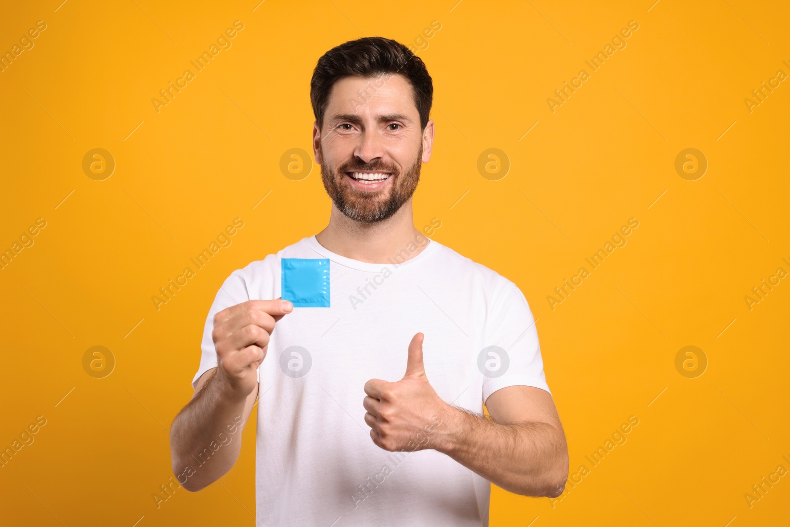 Photo of Happy man with condom showing thumb up on yellow background. Safe sex
