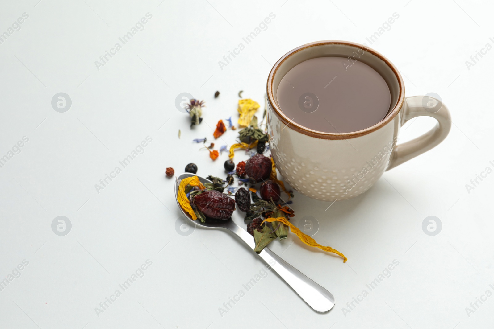 Photo of Cup of freshly brewed tea, dried herbs and spoon on white background