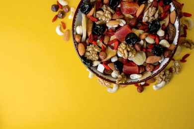 Photo of Bowl with mixed dried fruits and nuts on yellow background, flat lay. Space for text
