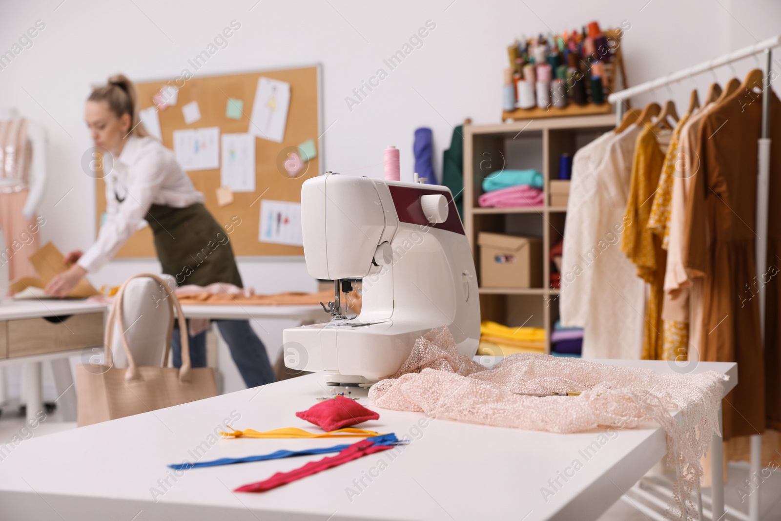 Photo of Dressmaker working in atelier, focus on table with sewing machine and accessories