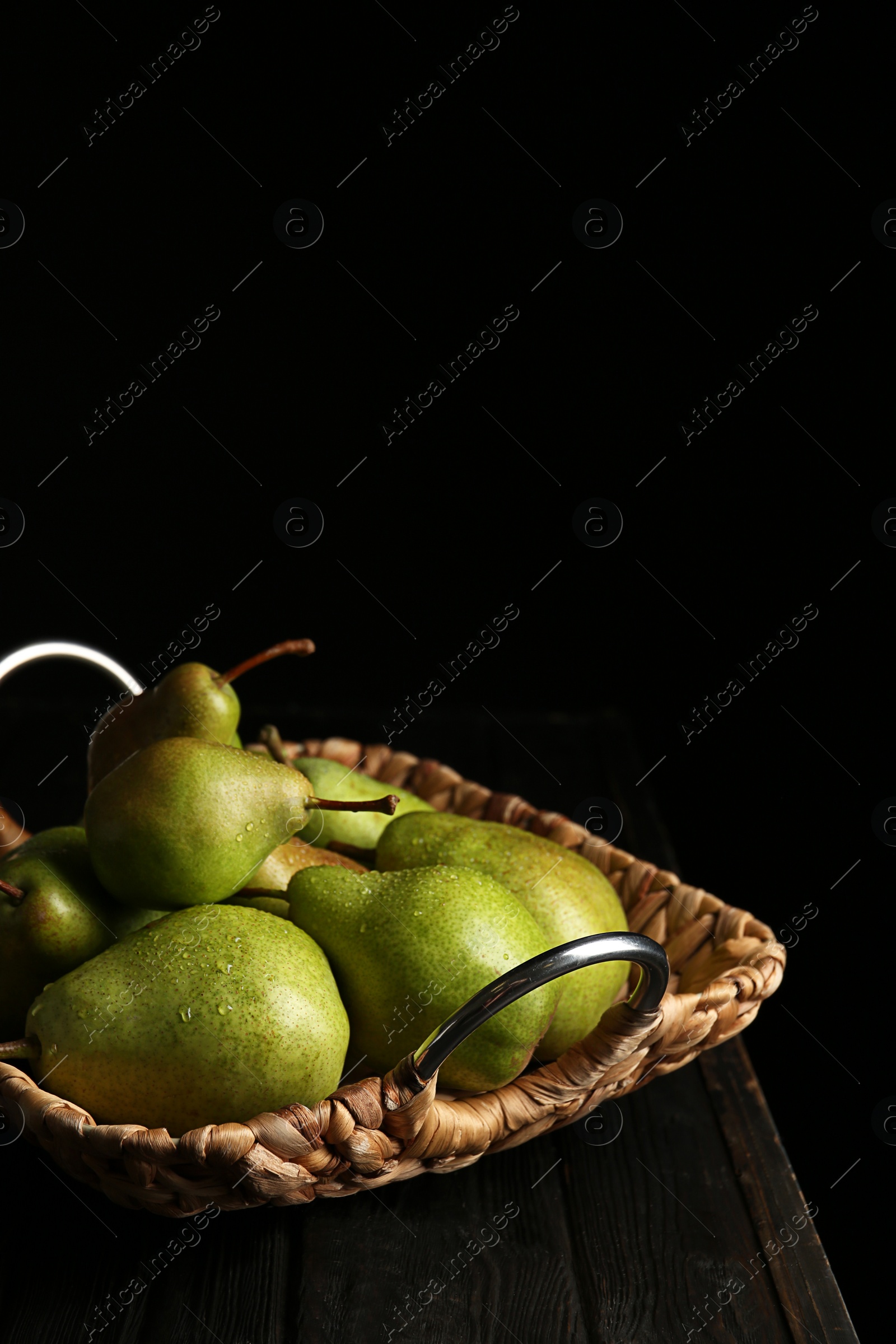 Photo of Tray with ripe pears on wooden table against dark background. Space for text