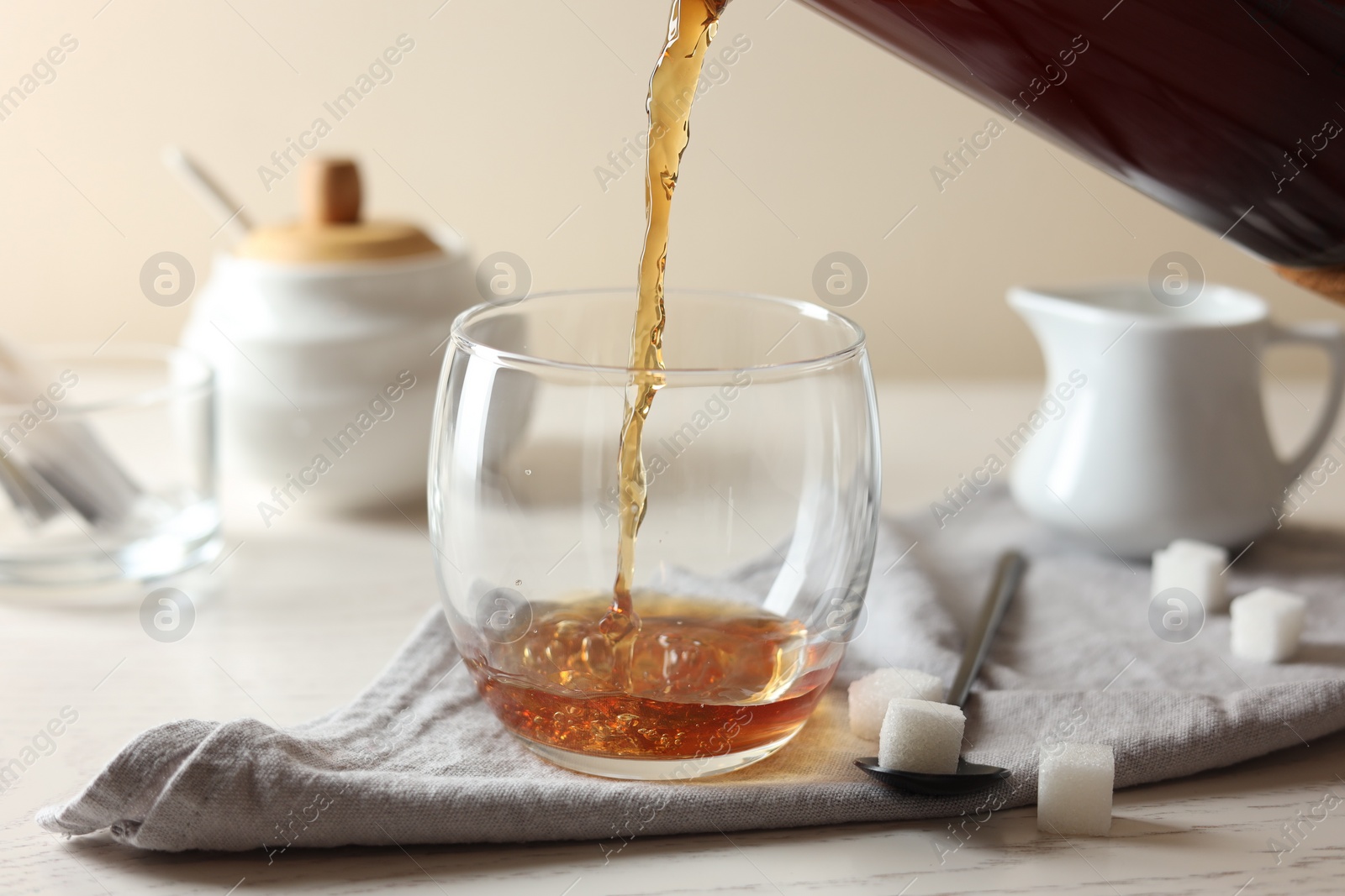 Photo of Pouring warm tea into cup on white wooden table, closeup