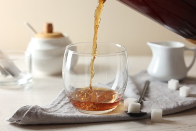 Photo of Pouring warm tea into cup on white wooden table, closeup