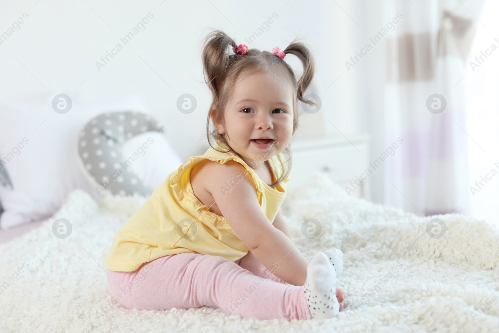 Photo of Adorable little baby girl sitting on bed in room