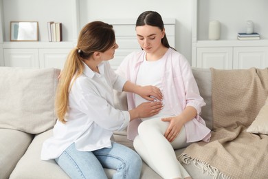 Doula taking care of pregnant woman on sofa at home. Preparation for child birth