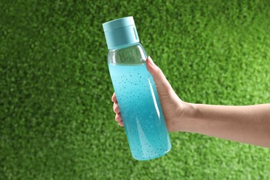 Photo of Woman holding bottle of light blue drink outdoors, closeup