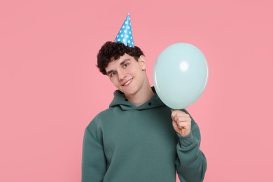 Young man in party hat with balloon on pink background