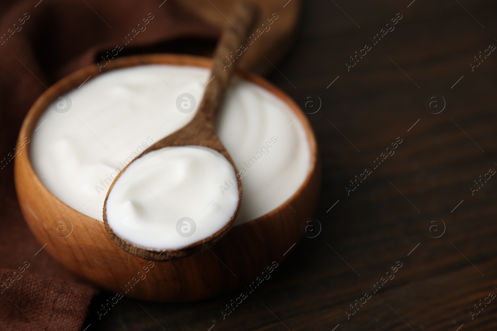 Photo of Delicious natural yogurt in bowl and spoon on wooden table, closeup. Space for text