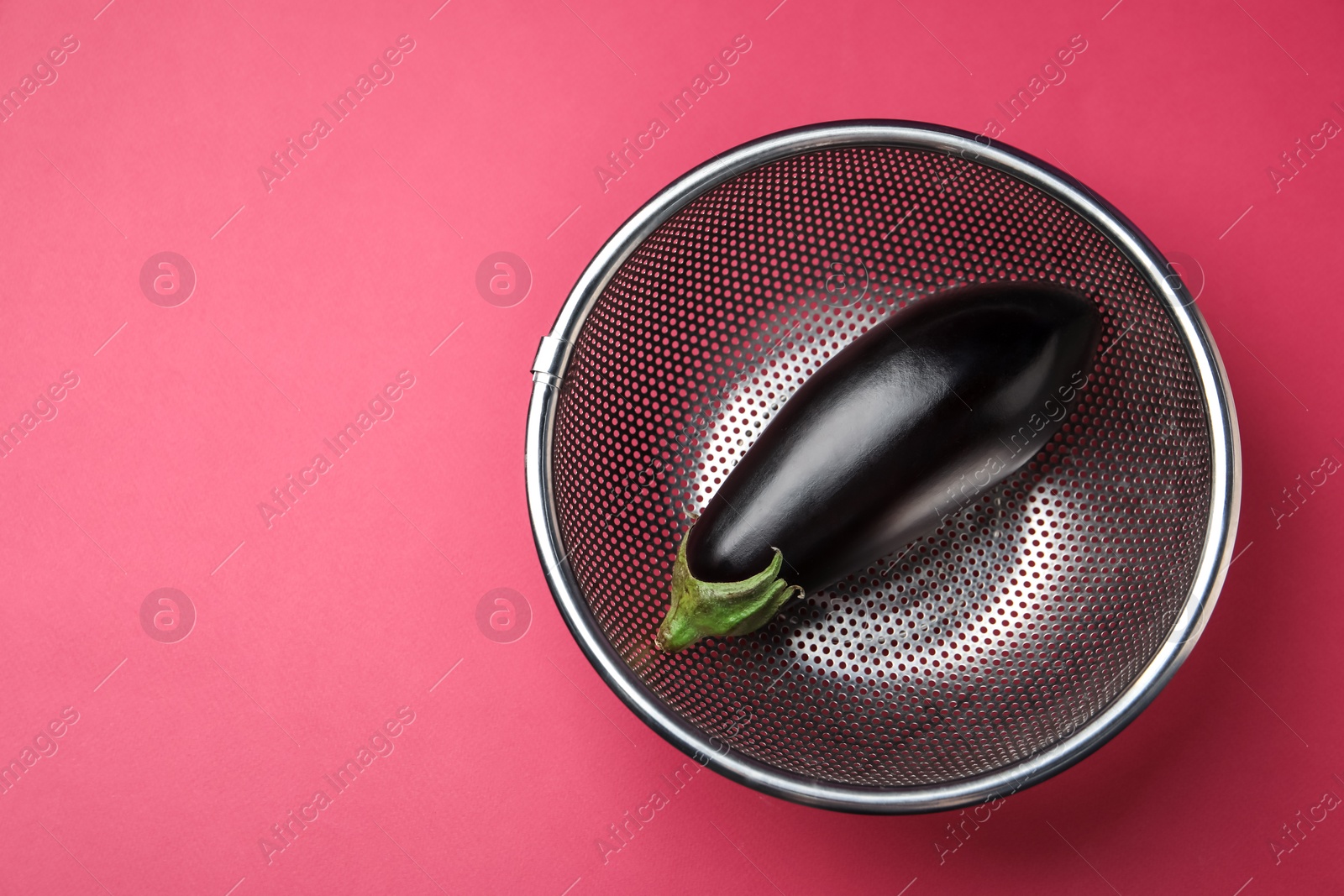 Photo of Colander with fresh eggplant on pink table, top view. Space for text