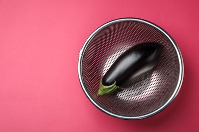 Photo of Colander with fresh eggplant on pink table, top view. Space for text