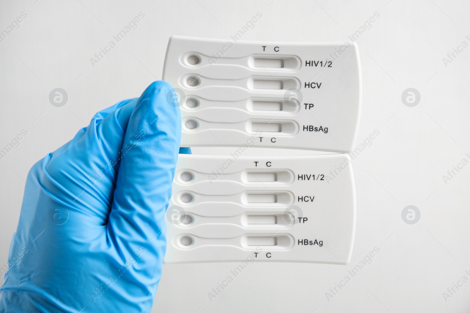 Photo of Doctor in gloves holding disposable express tests for hepatitis on white background, closeup