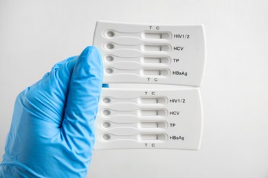 Photo of Doctor in gloves holding disposable express tests for hepatitis on white background, closeup