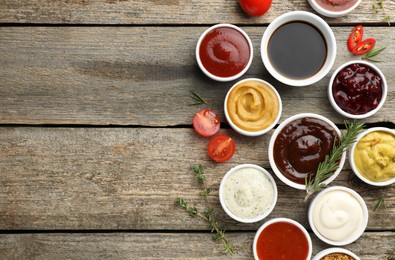 Photo of Different tasty sauces in bowls and ingredients on wooden table, flat lay. Space for text