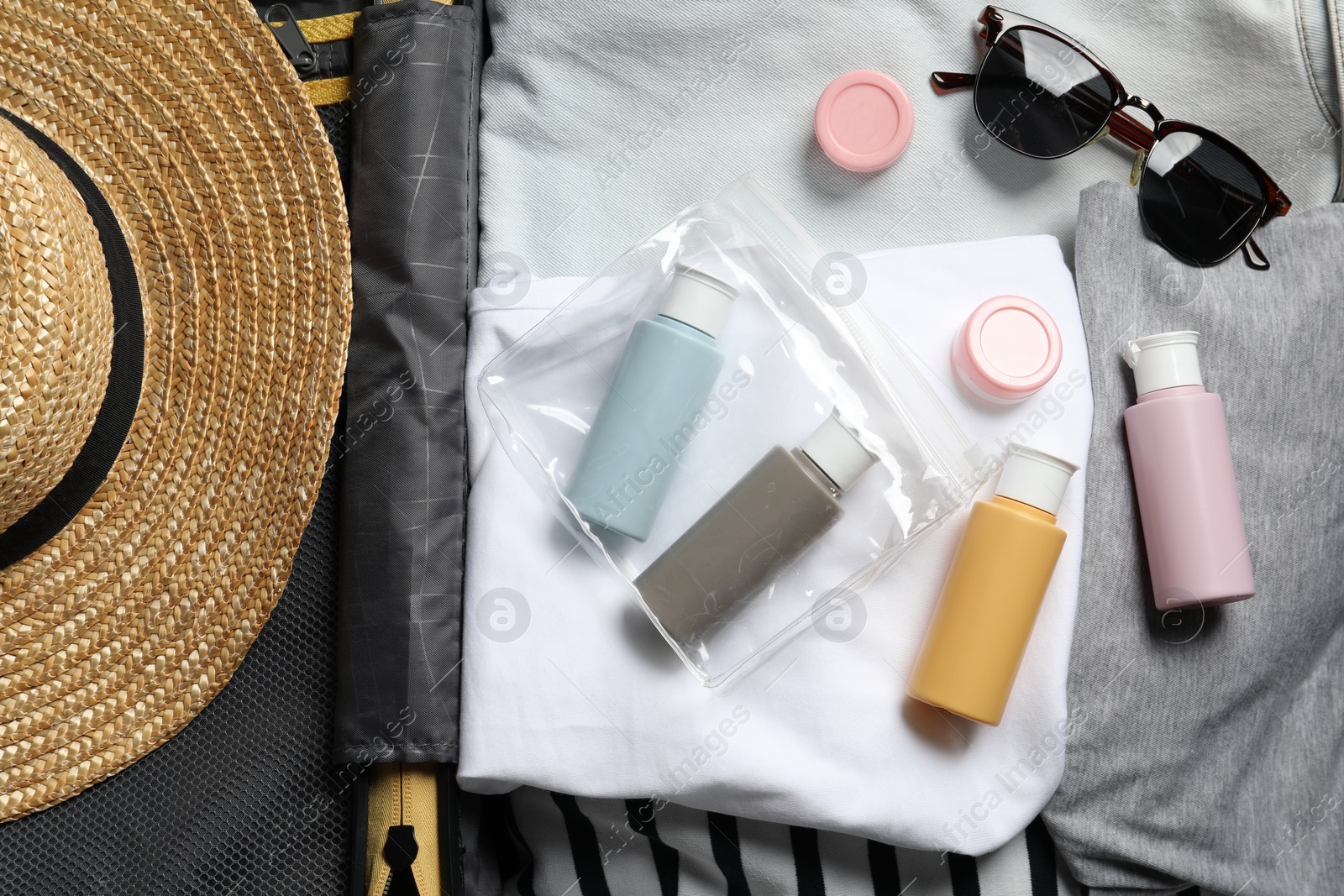 Photo of Cosmetic travel kit, plastic bag and accessories in suitcase, top view