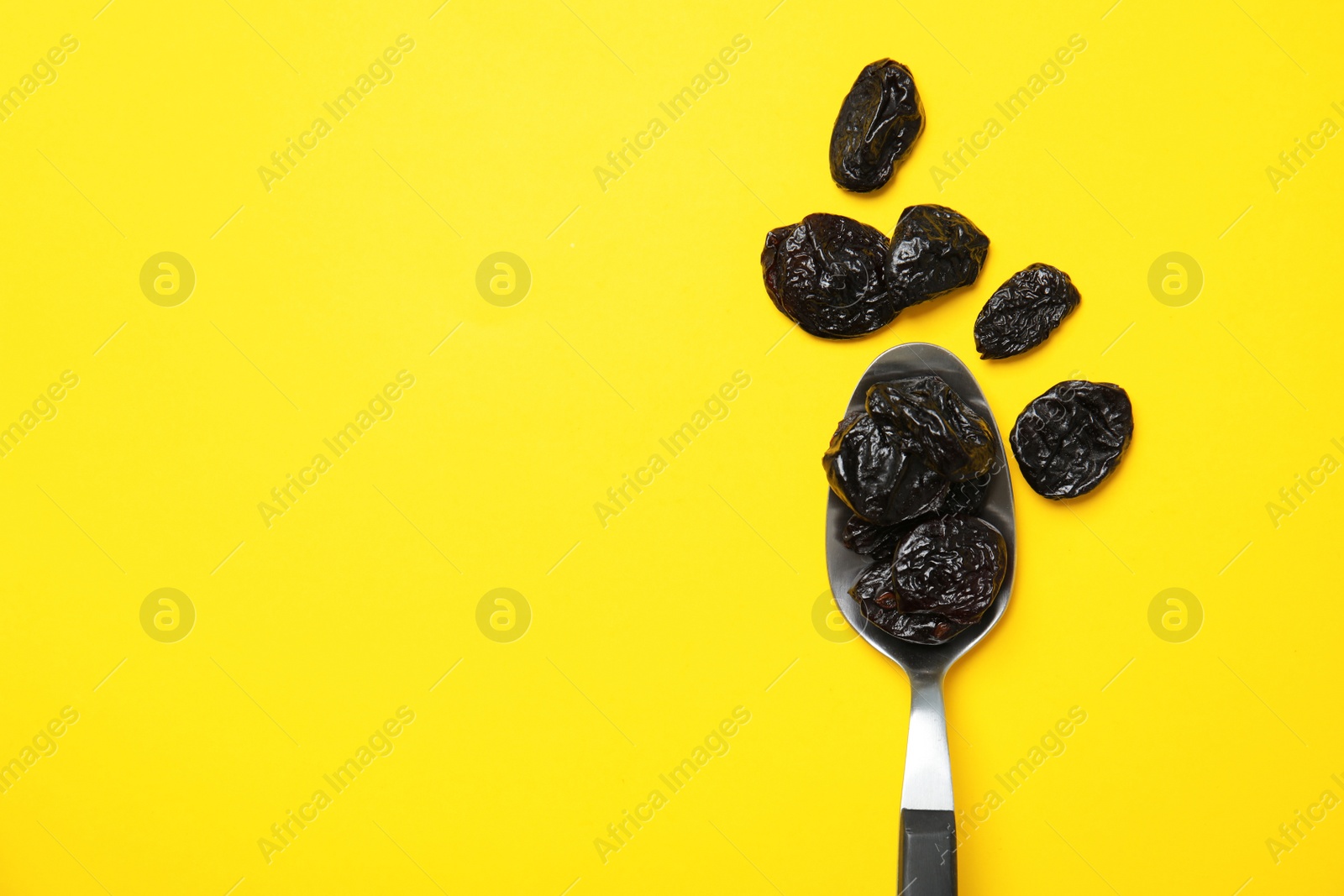 Photo of Spoon of dried plums on color background, top view with space for text. Healthy fruit